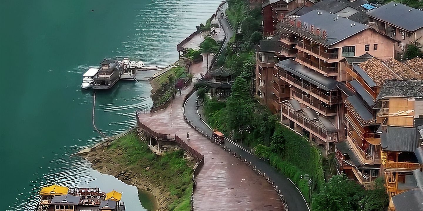 Tall wooden houses of Gongtan Ancient Town stacked above the green Wujiang River, with a riverside walkway and moored boats