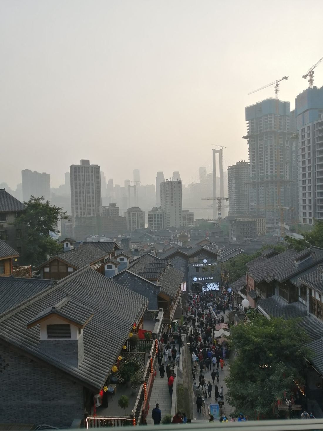 Looking down over the tiled roofs and the busy stone stairway of Shibati, with city towers in the haze behind